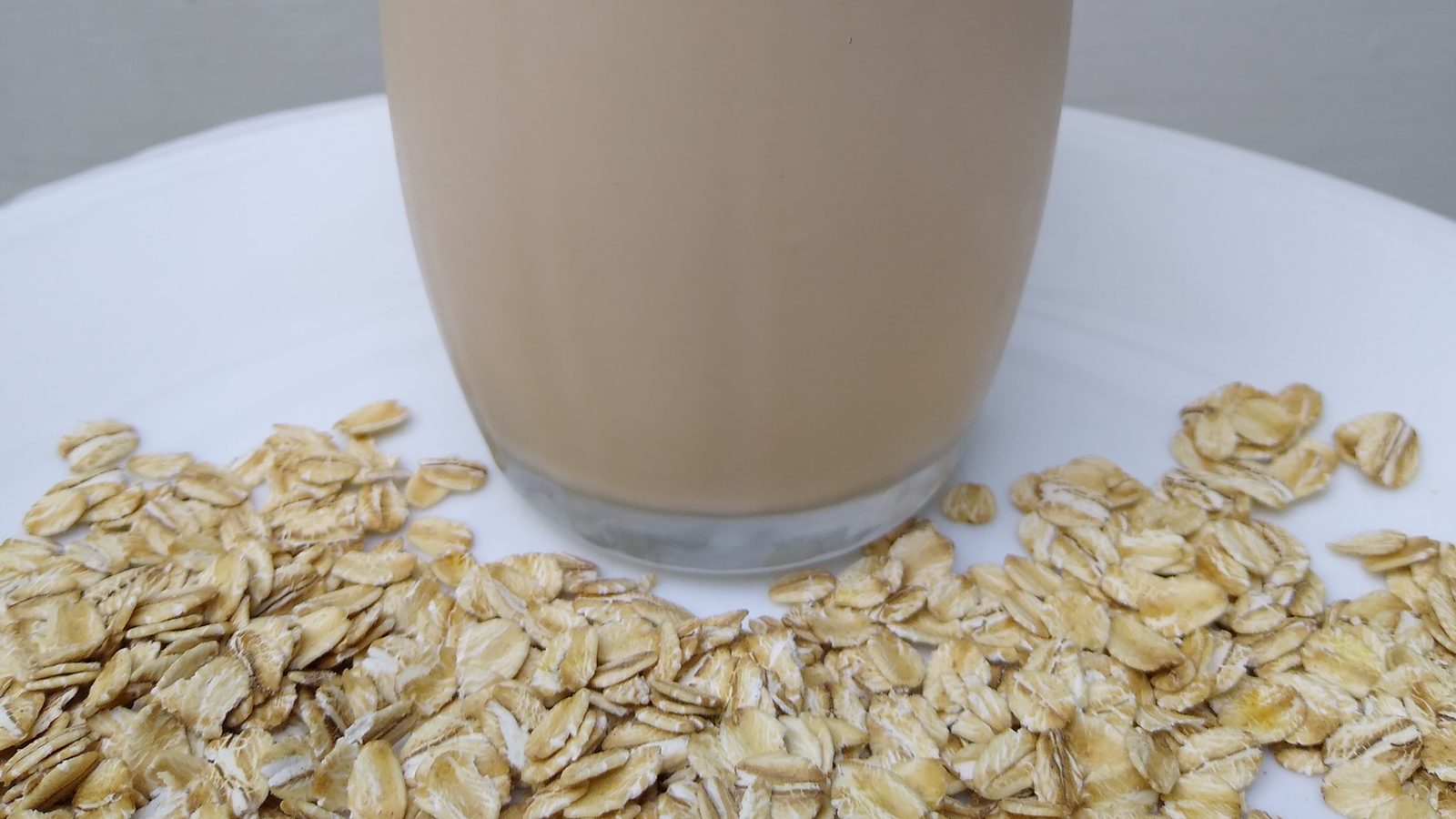 A glass of oat milk beside a bowl of rolled oats