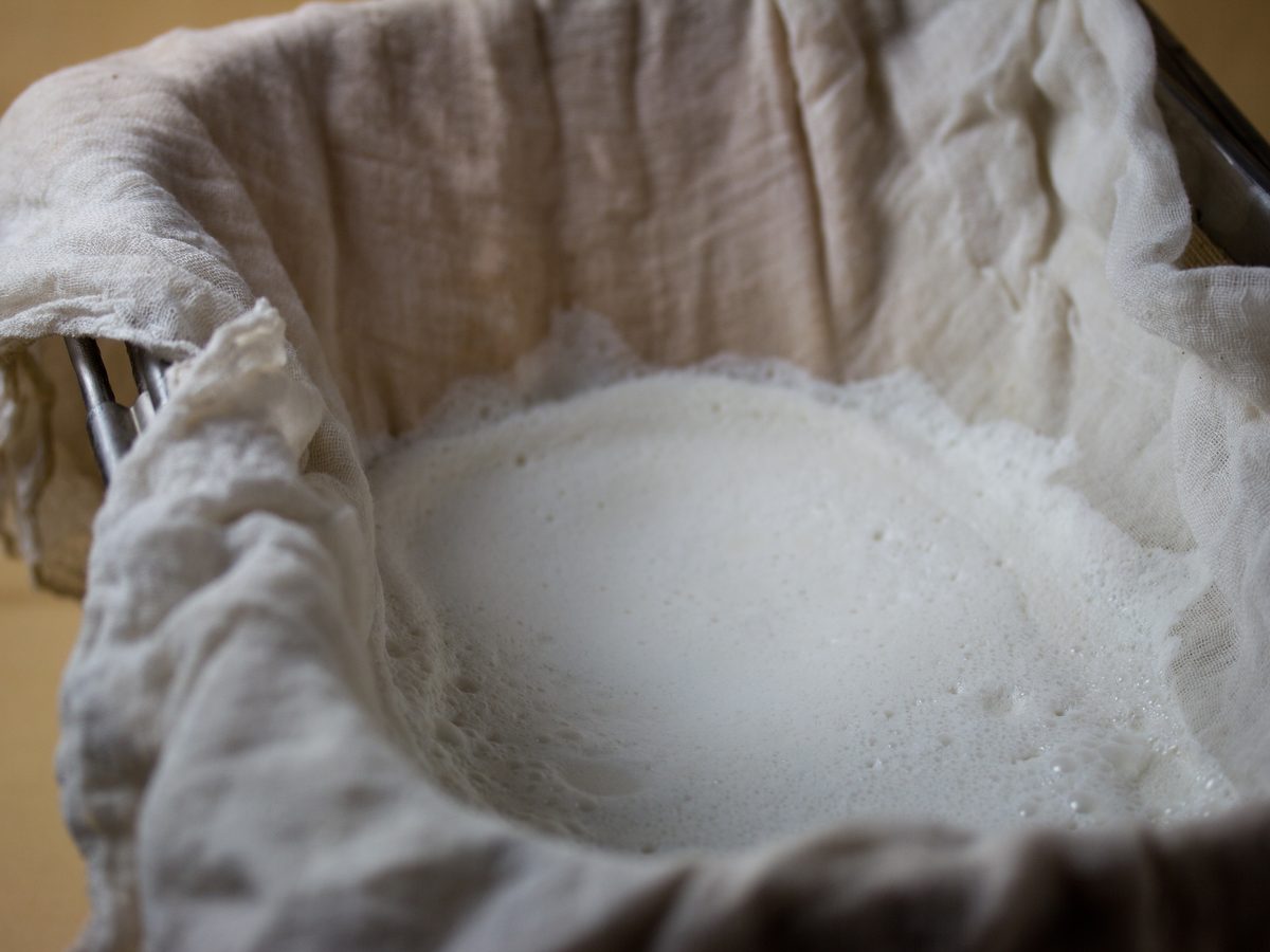 Almond milk being strained through a nut milk bag from a blender